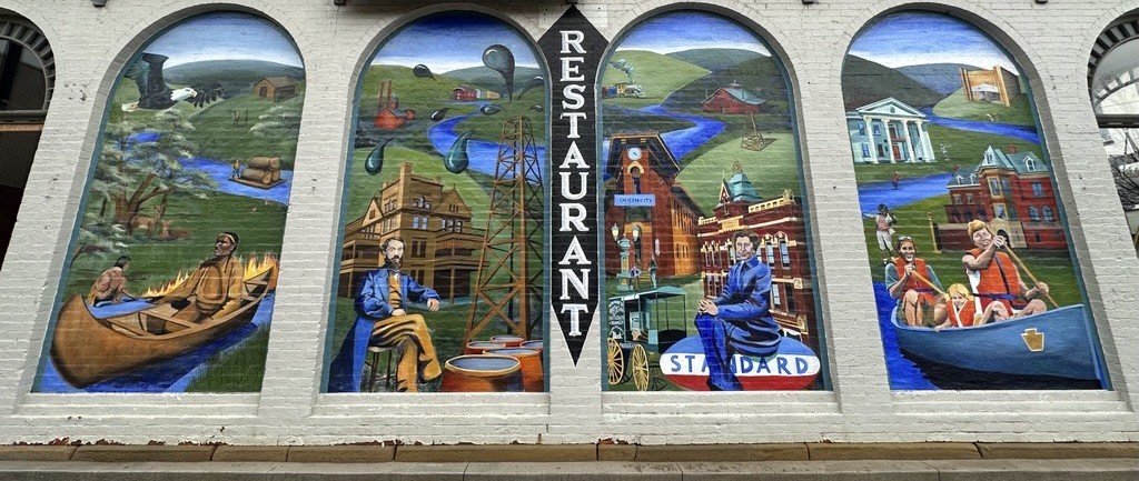 From left to right, the mural shows Native Americans and logging before the oil boom; “Colonel” Edwin Drake and an oil derrick; Standard Oil offices and local “muckraker” Ida Tarbell; and a family canoeing.