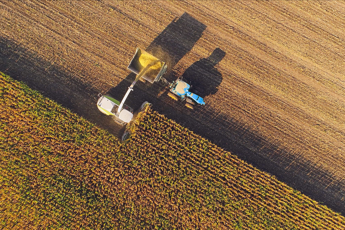 Arial photo of corn farm, with a tractor harvesting corn.
