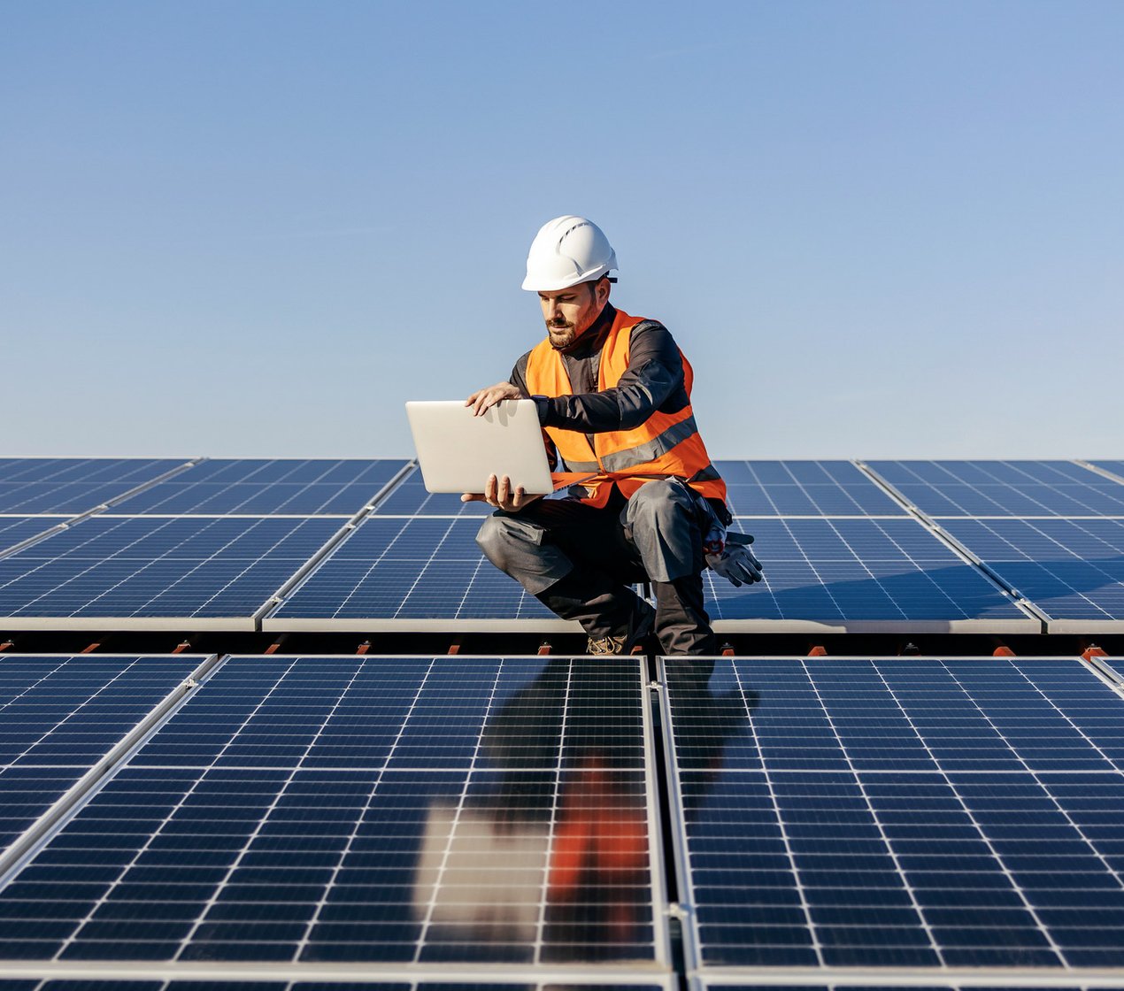 A handyman looking at the laptop on rooftop testing solar panels