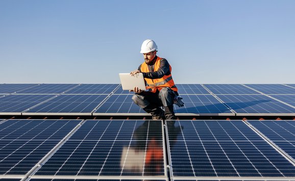 A handyman looking at the laptop on rooftop testing solar panels