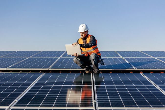 A handyman looking at the laptop on rooftop testing solar panels