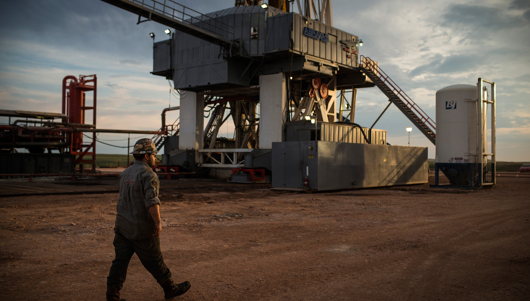 An oil worker walking in front of an oil drill at sunset