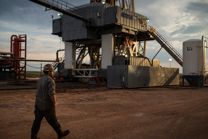 An oil worker walking in front of an oil drill at sunset