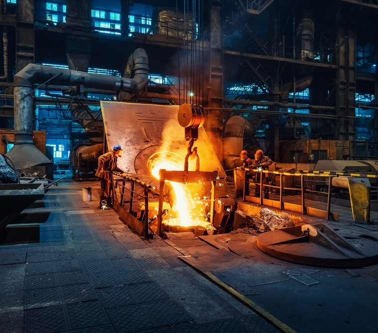 Workers around a furnace in metallurgical plant or factory, with liquid iron molten metal pouring in container