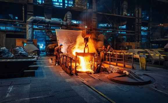Workers around a furnace in metallurgical plant or factory, with liquid iron molten metal pouring in container