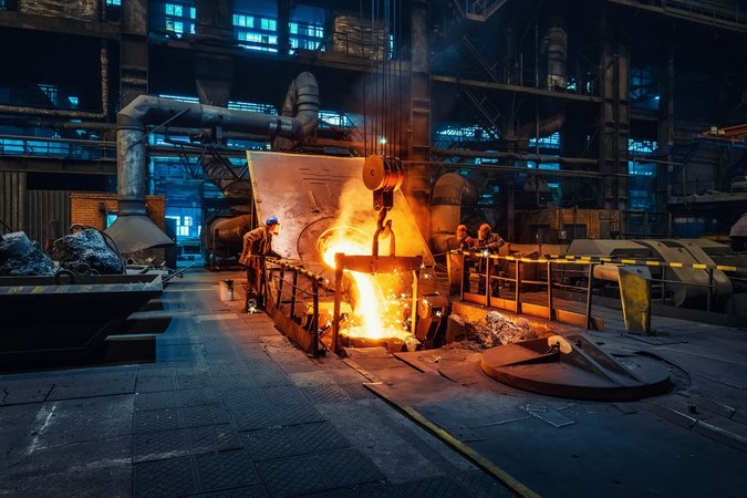 Workers around a furnace in metallurgical plant or factory, with liquid iron molten metal pouring in container