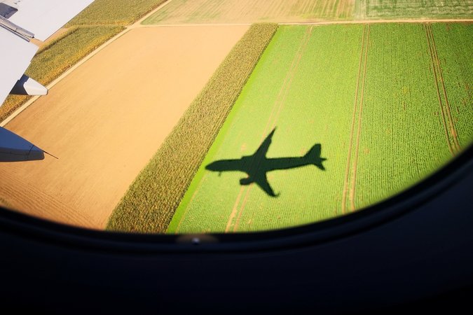Aeriel view of an airplane shadow looking out of an airplane window over a field
