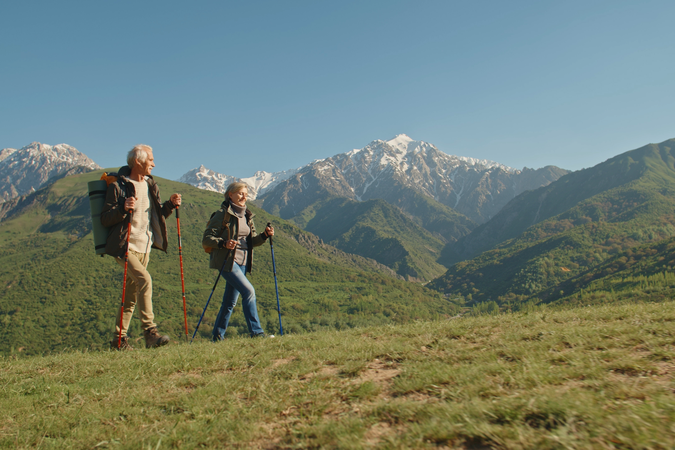 Couple hiking on grassy mountain tops on a sunny day.
