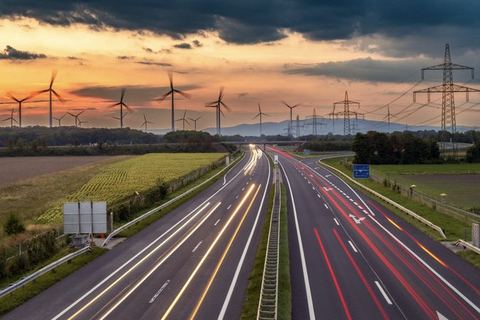 Long-exposure image of cars driving on highway with farms, powerlines, and wind turbines in the background