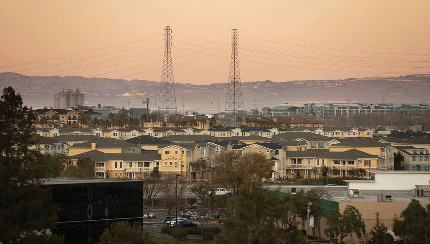 Sunset view of a dense housing neighborhood of Redwood City, California, USA, with electrical transmission towers in the background