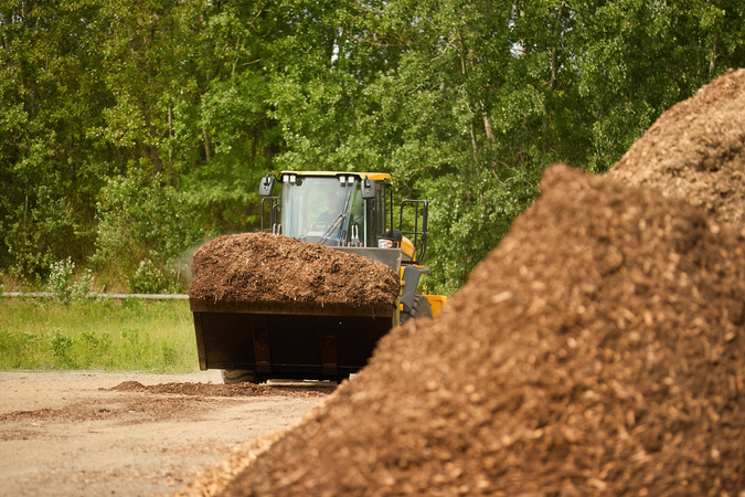Excavator loading biomass fuel for a multi-fuel boiler in the outskirts of a forest.