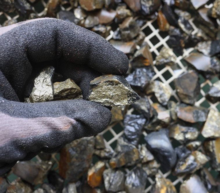 Gloved hand holding cassiterite, the world’s most important ore of tin, typically appearing as heavy, brown‑to‑black crystals found in granites and placer deposits