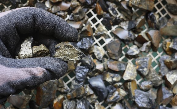 Gloved hand holding cassiterite, the world’s most important ore of tin, typically appearing as heavy, brown‑to‑black crystals found in granites and placer deposits