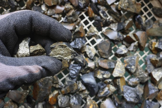 Gloved hand holding cassiterite, the world’s most important ore of tin, typically appearing as heavy, brown‑to‑black crystals found in granites and placer deposits