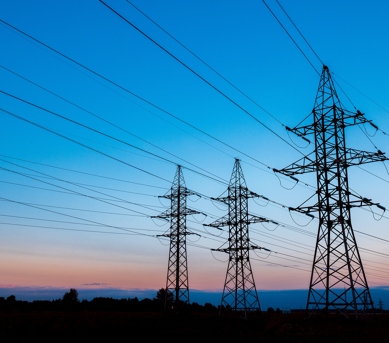 Three high-voltage power lines against a blue and orange sunset.