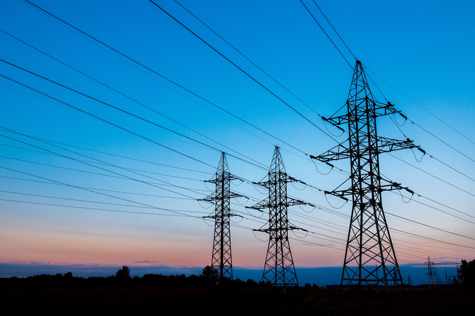 Three high-voltage power lines against a blue and orange sunset.