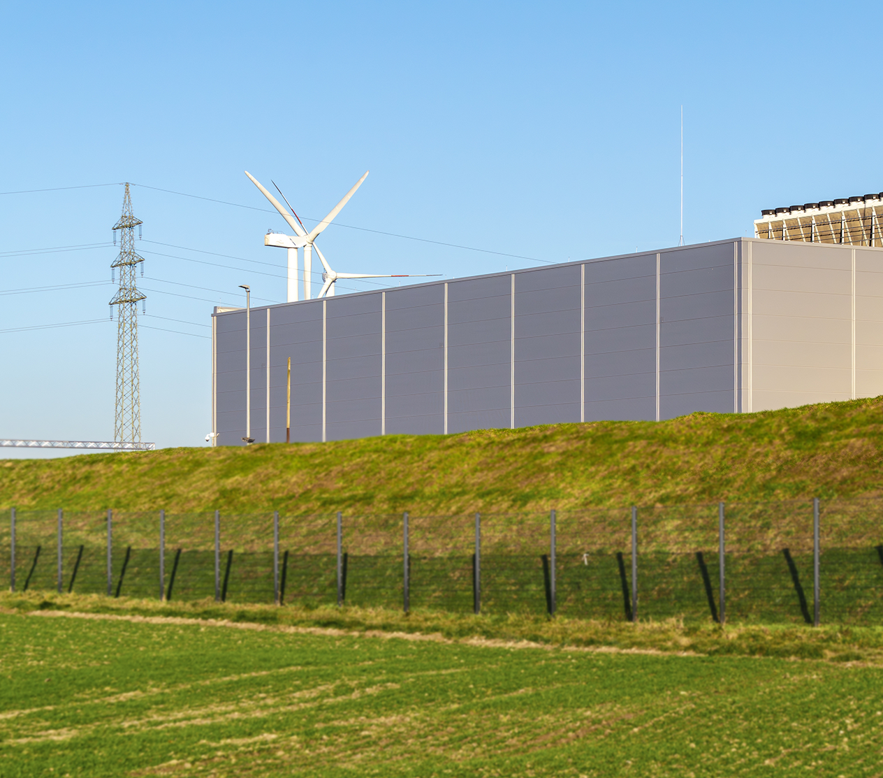 Large data center building with windmills in the background on a sunny day