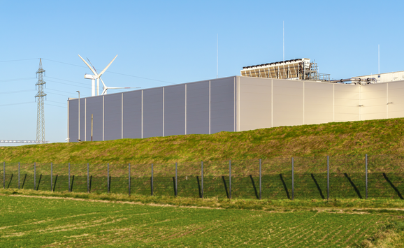 Large data center building with windmills in the background on a sunny day