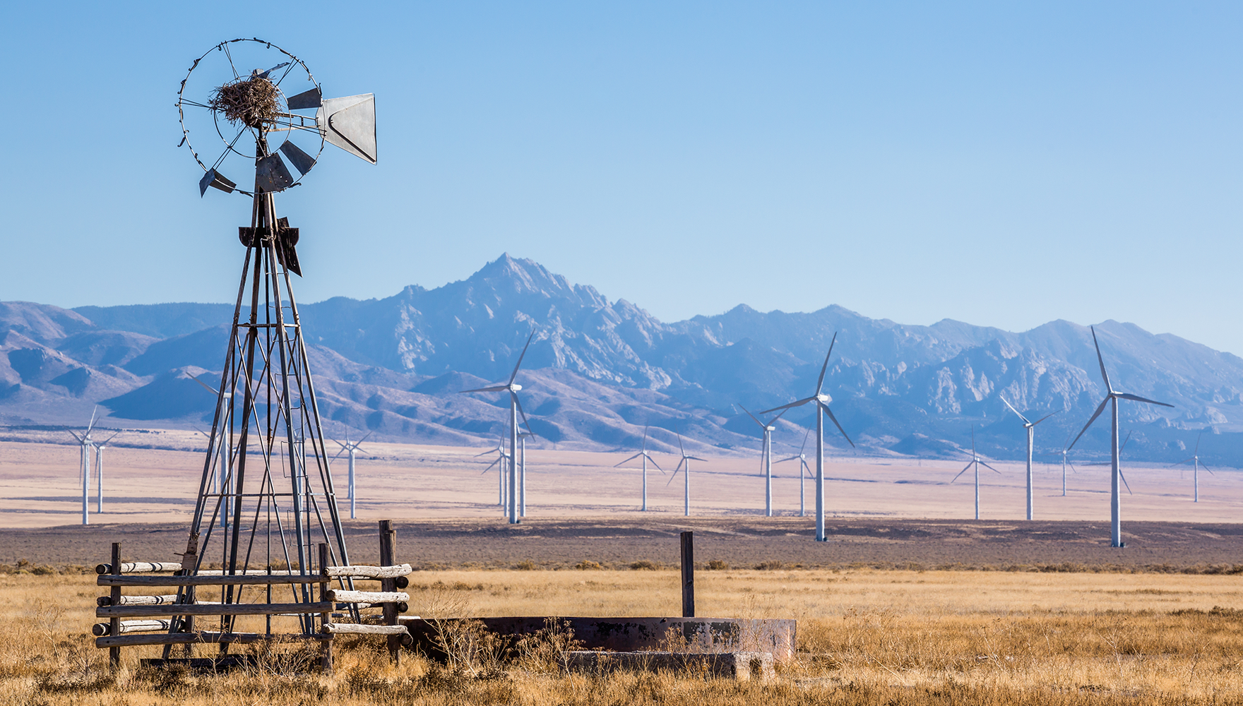 An wind farm in a Utah valley in the background of an old, wooden windmill