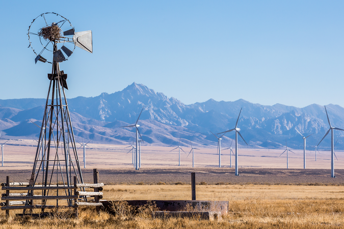 An wind farm in a Utah valley in the background of an old, wooden windmill